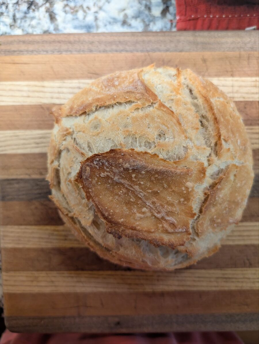 A rustic scored loaf of artisan bread on a striped wooden cutting board